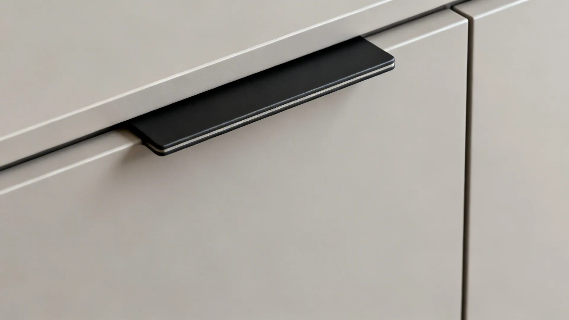 Close-up of a slim black tab pull on a matte slab cabinet door edge.