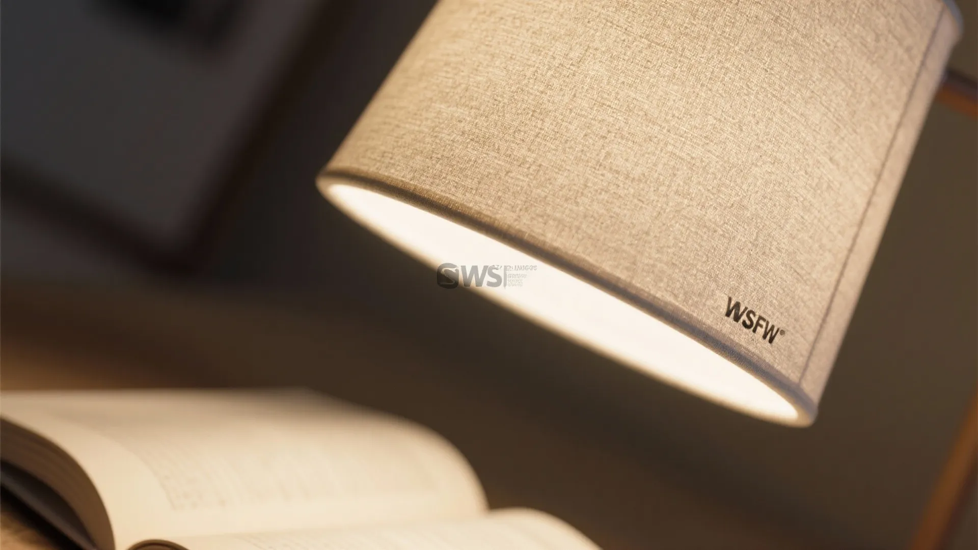 Close up view of a desk light with fabric shade illuminating an open book at night