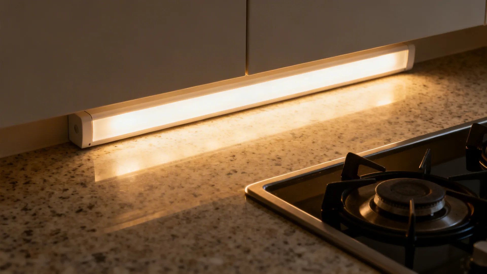 Macro of warm under-cabinet LED light evenly illuminating a quartz countertop by a hob.