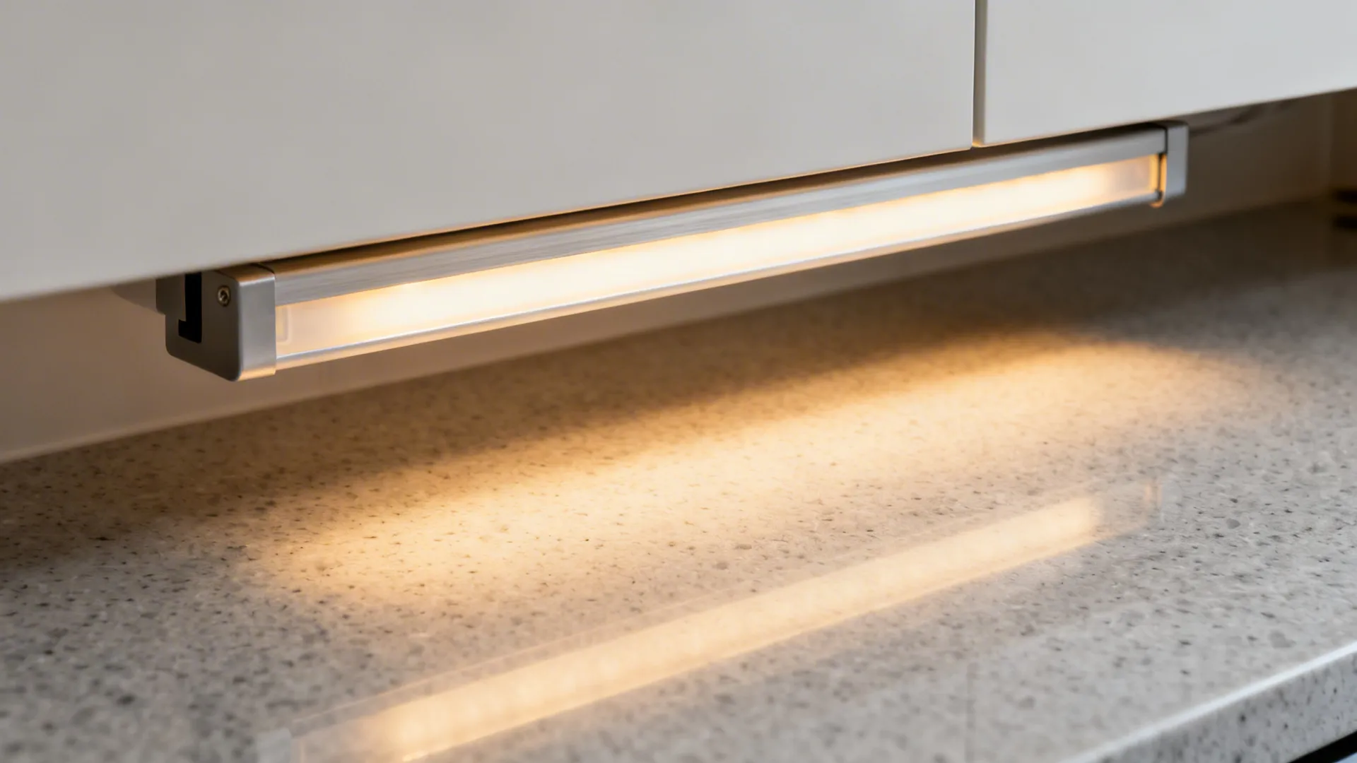 Under cabinet light fixture illuminating a grey speckled kitchen countertop with a warm yellow glow