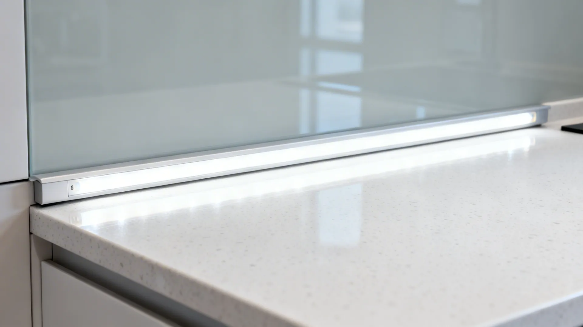 Macro of under-cabinet LED light illuminating white quartz and reflecting on a glass backsplash.