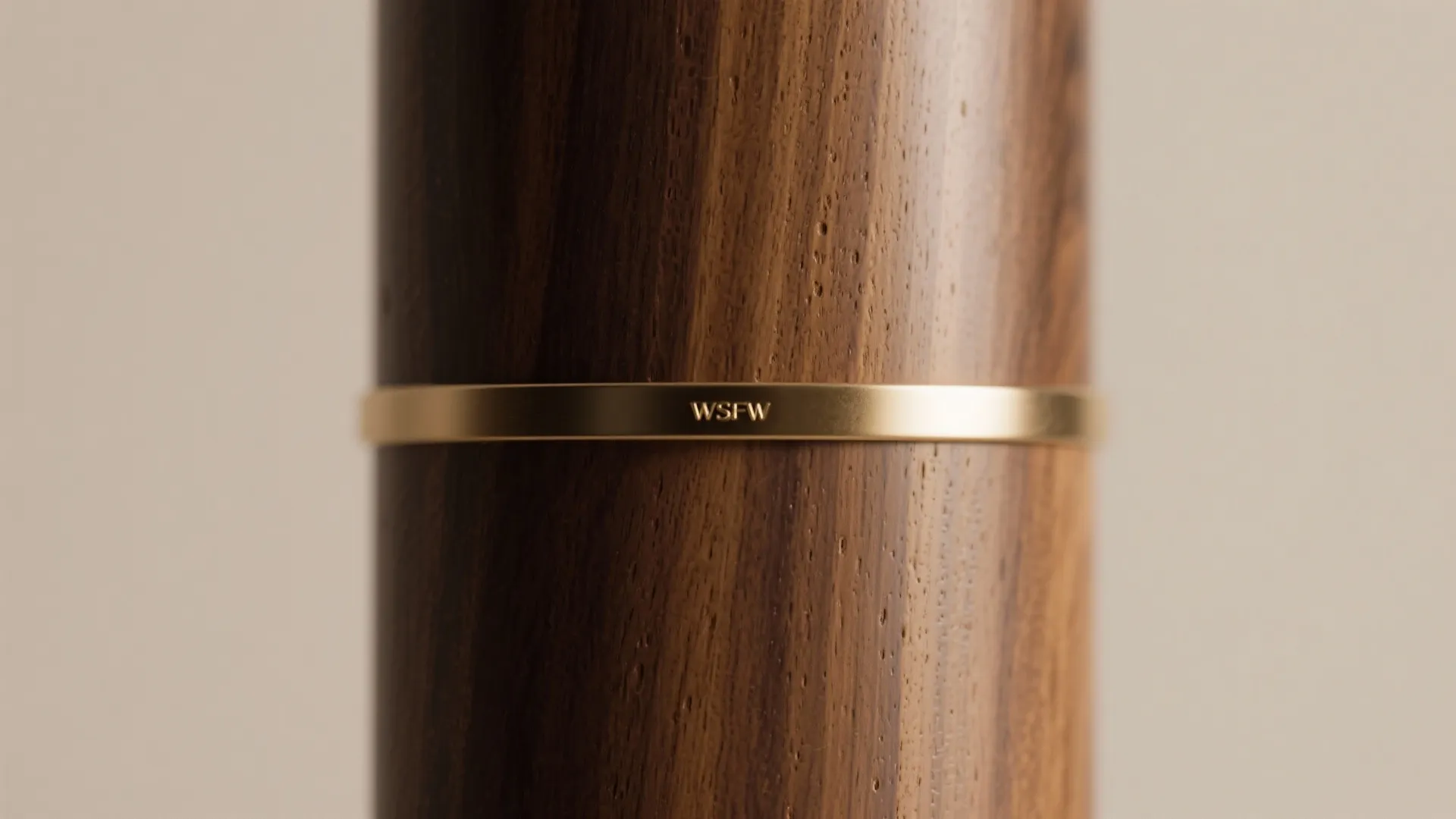 Close-up of teak veneer with a brushed brass band in soft warm daylight.