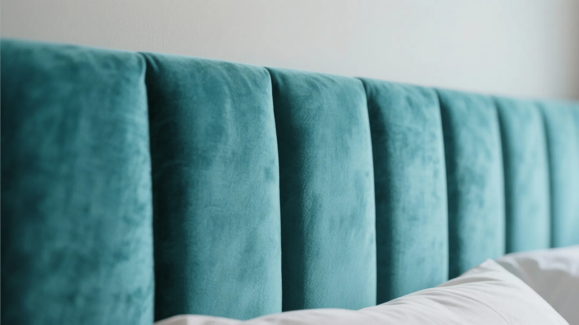 Close up of a soft teal velvet padded headboard with vertical panels in a bedroom