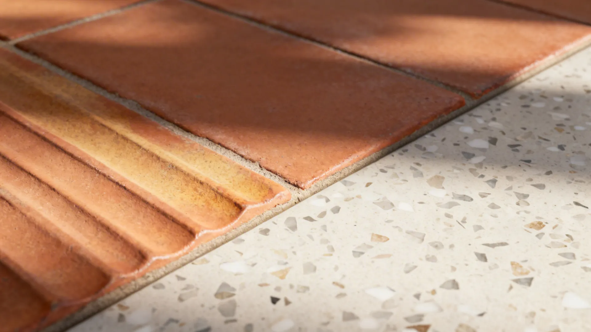Macro of ridged terracotta tile beside fine-chip porcelain terrazzo floor.