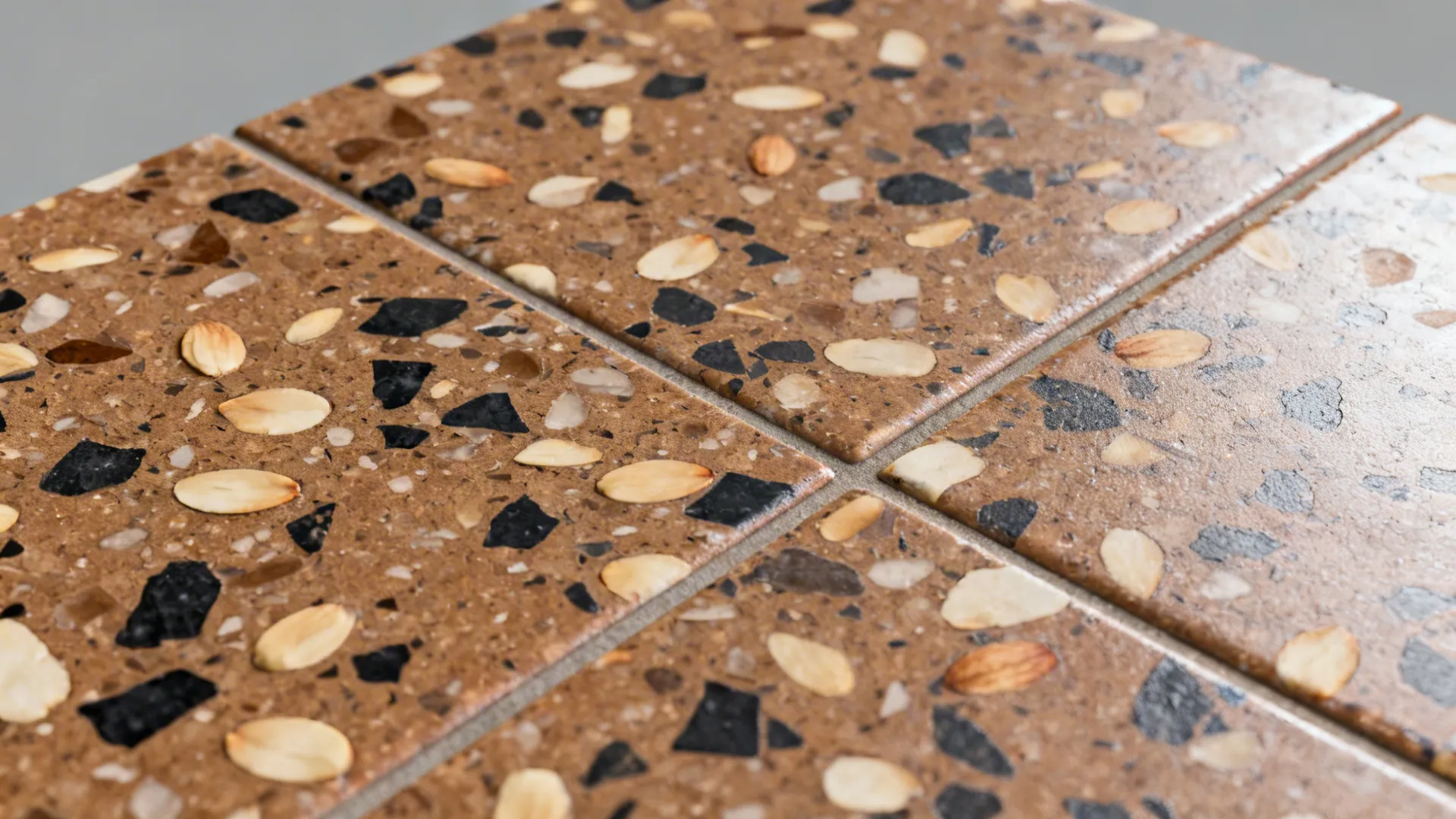 Top-down macro of mid-brown terrazzo showing almond and charcoal chips and clean grout.