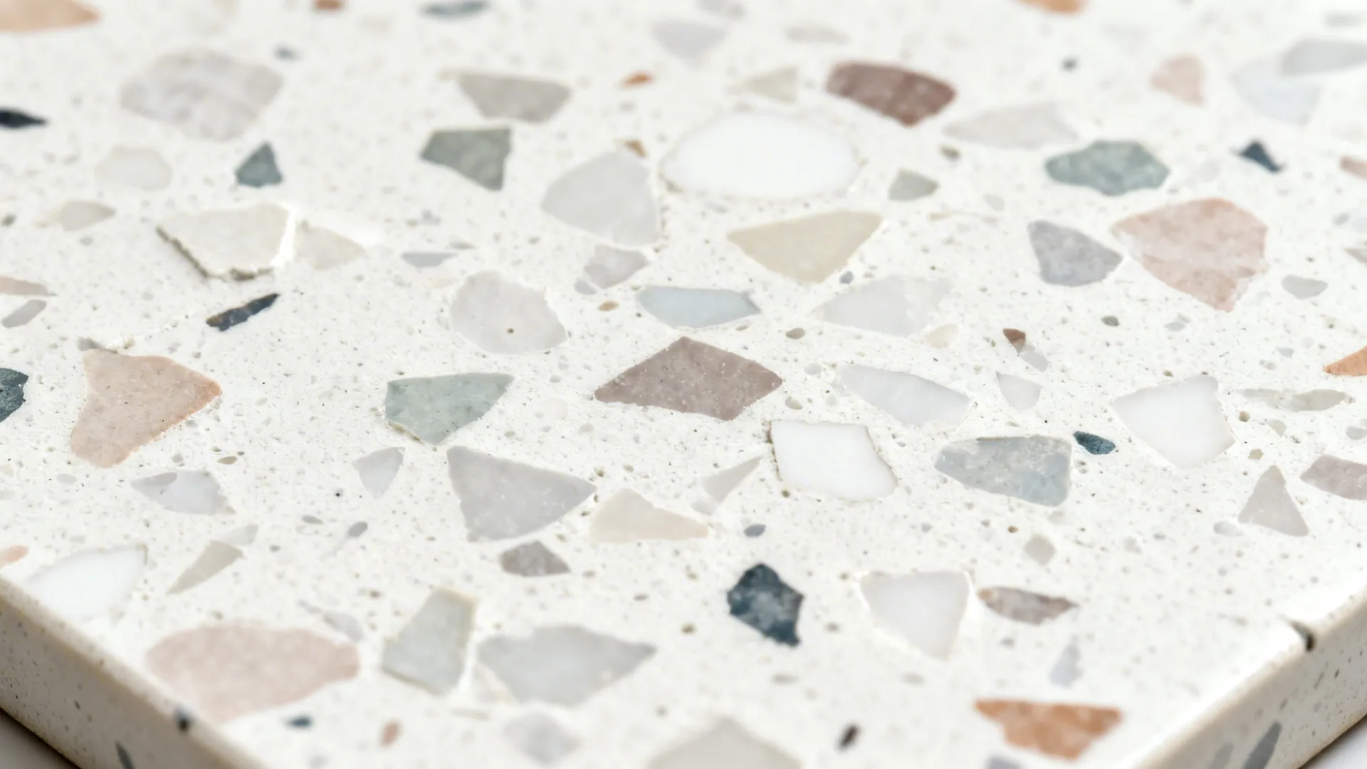 Macro of terrazzo-look porcelain with soft white base and muted mid-size chips in matte finish.