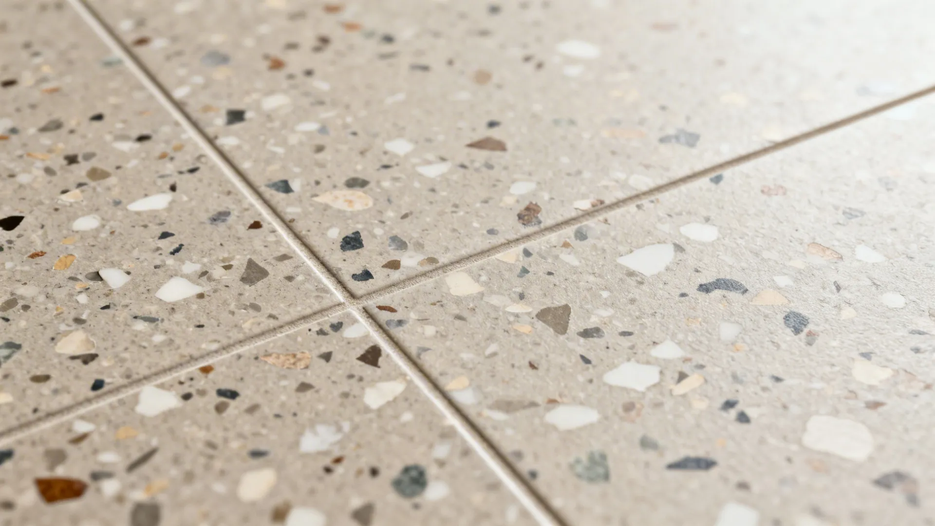 Close up of light grey floor tiles with colorful small stone pieces and thin grey lines