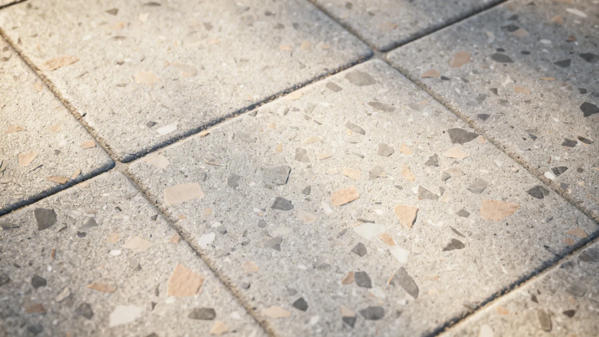 Macro of matte terrazzo-look porcelain with warm gray and taupe chips and tight grout.