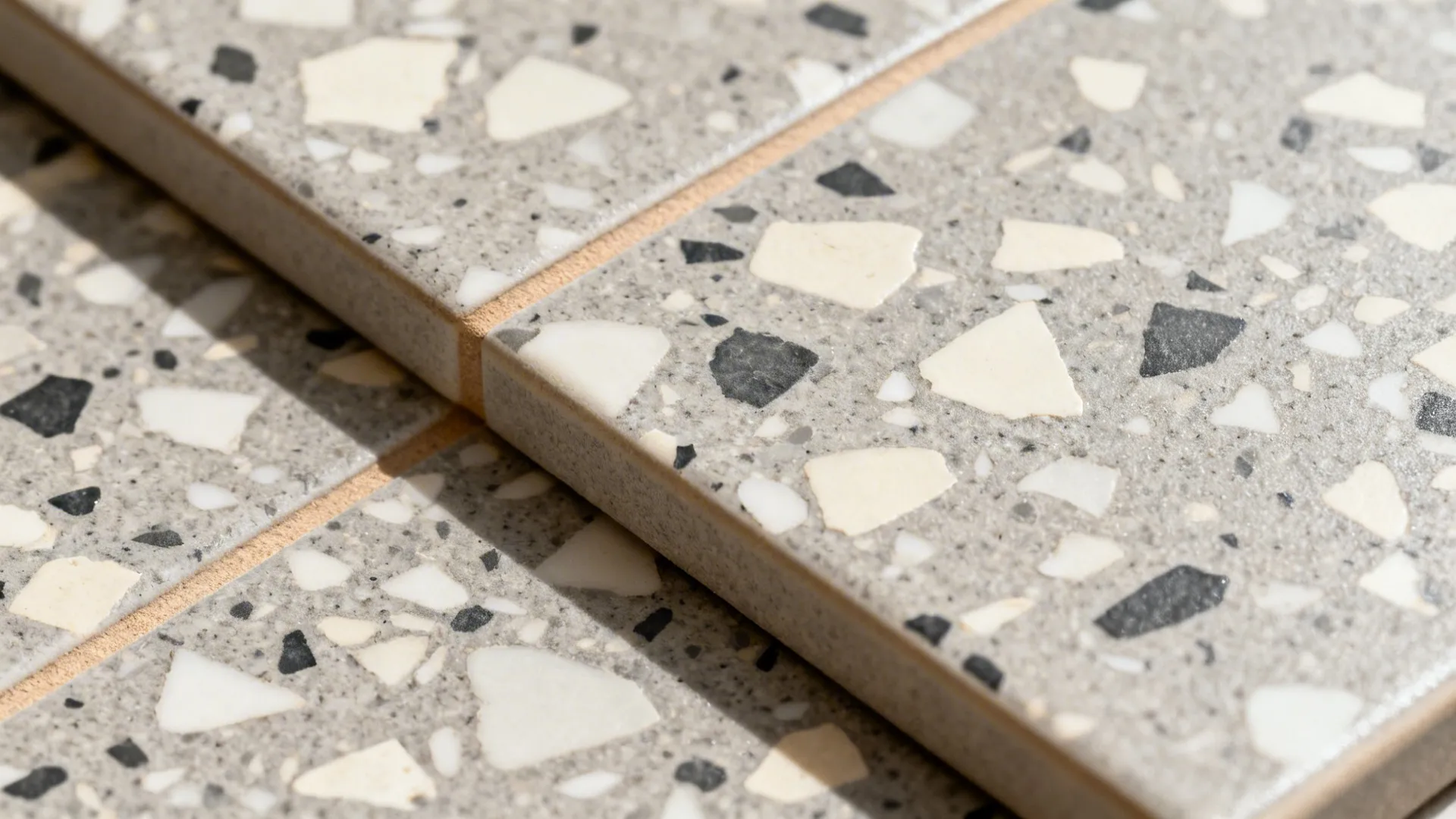 Macro of warm-grey terrazzo-look porcelain with ivory and charcoal chips and warm grout.