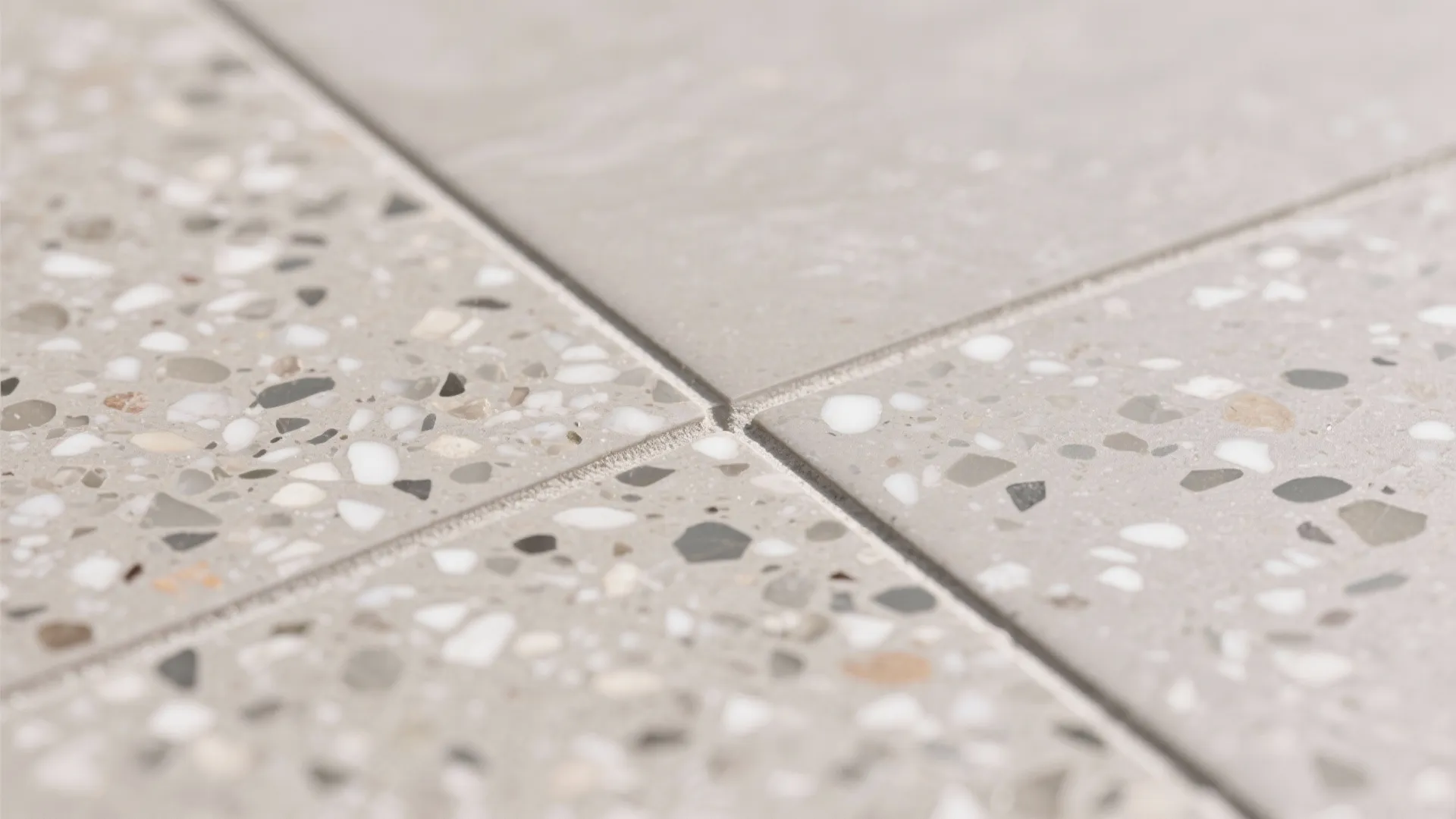 Close up view of grey floor tiles with small colorful stone pieces and thin grout lines