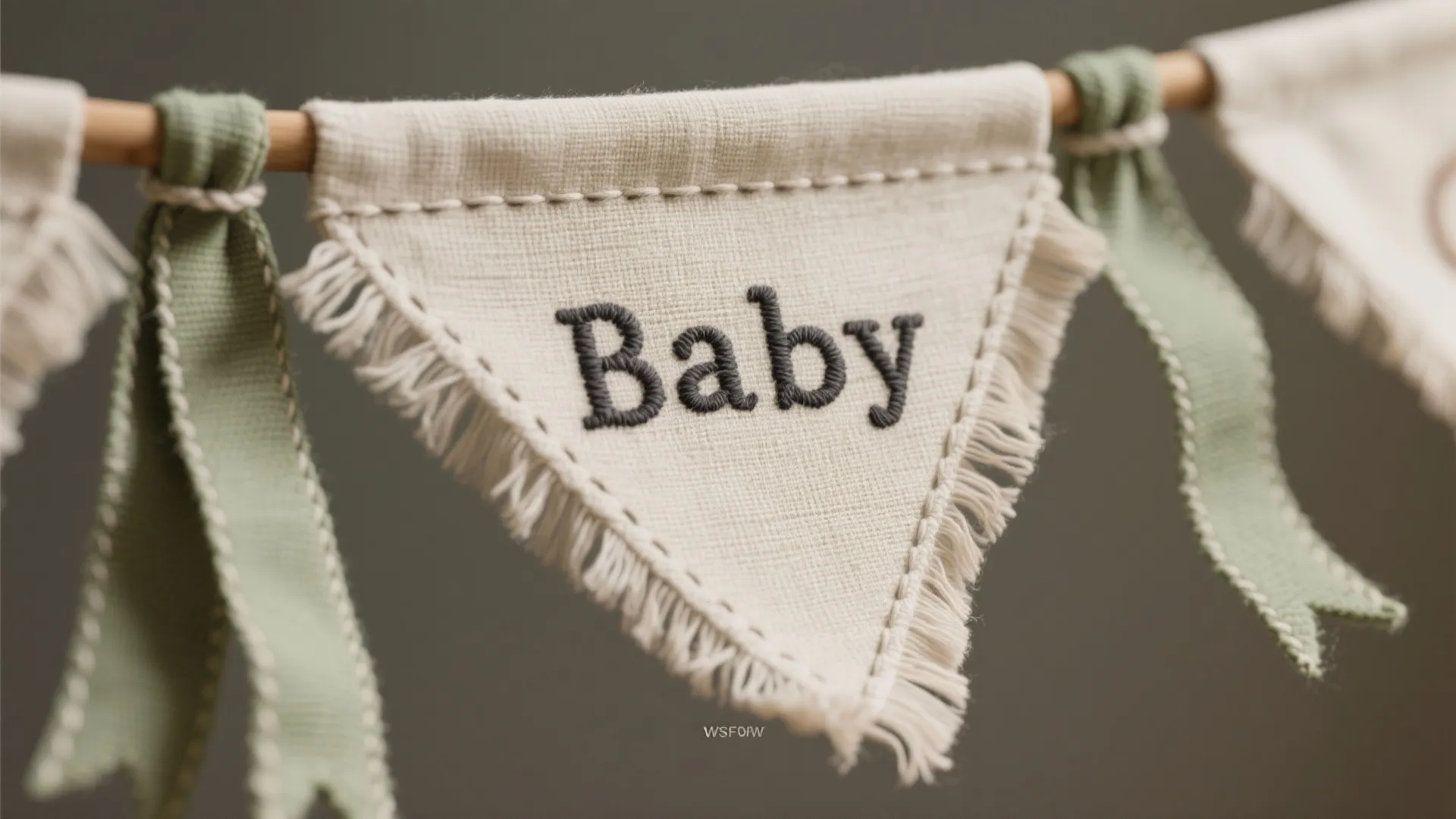 Macro of linen pennant banner with hand-embroidered baby name letters, soft tassels, and muted ribbons.