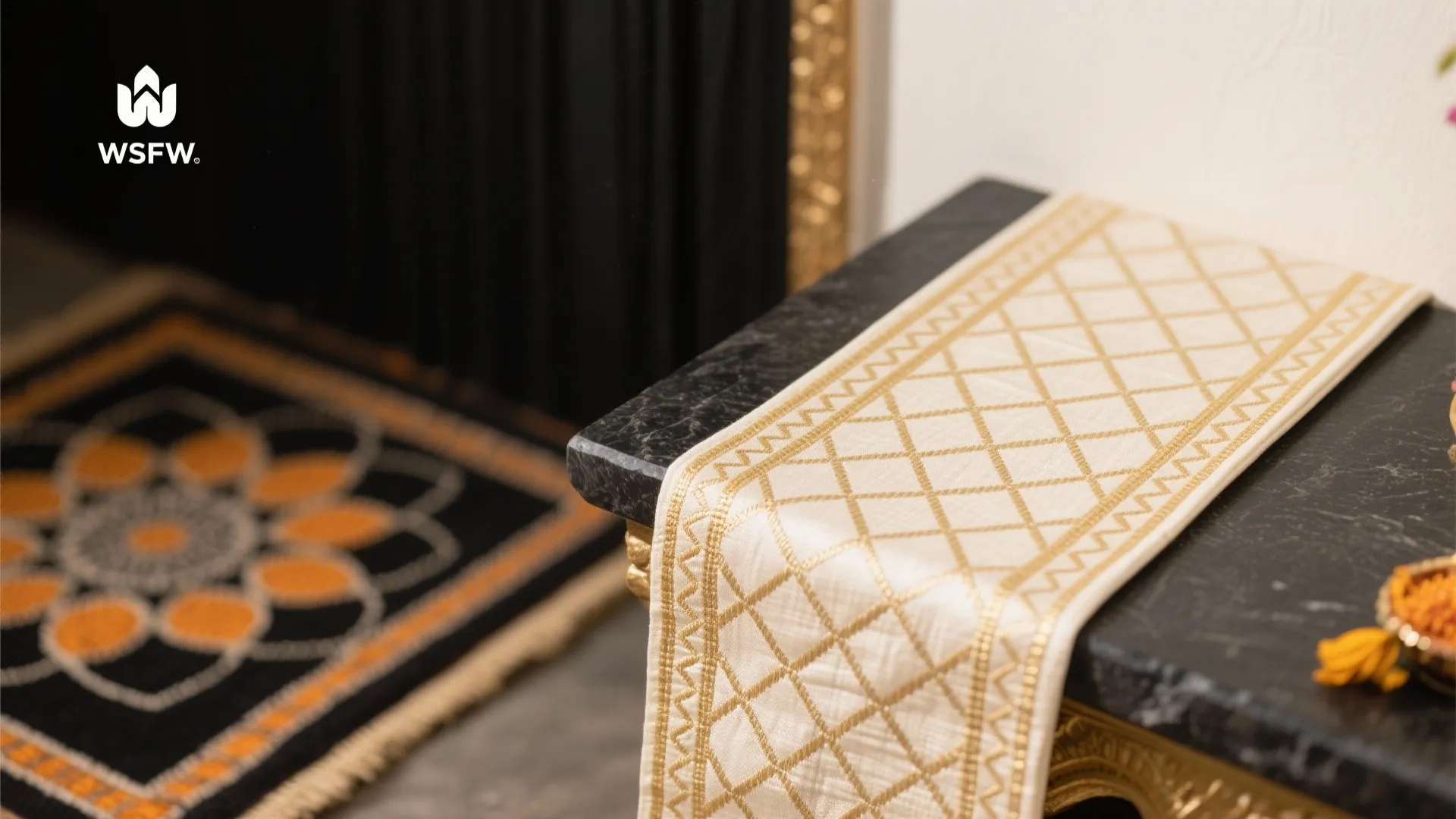 White table runner with gold diamond pattern on black marble table next to patterned rug