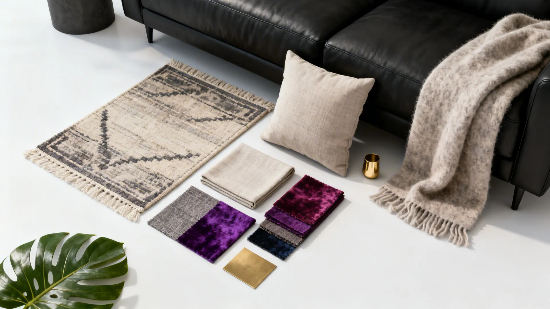 Flatlay of rug and cushion samples, throws and a brass accent for styling a black sofa.