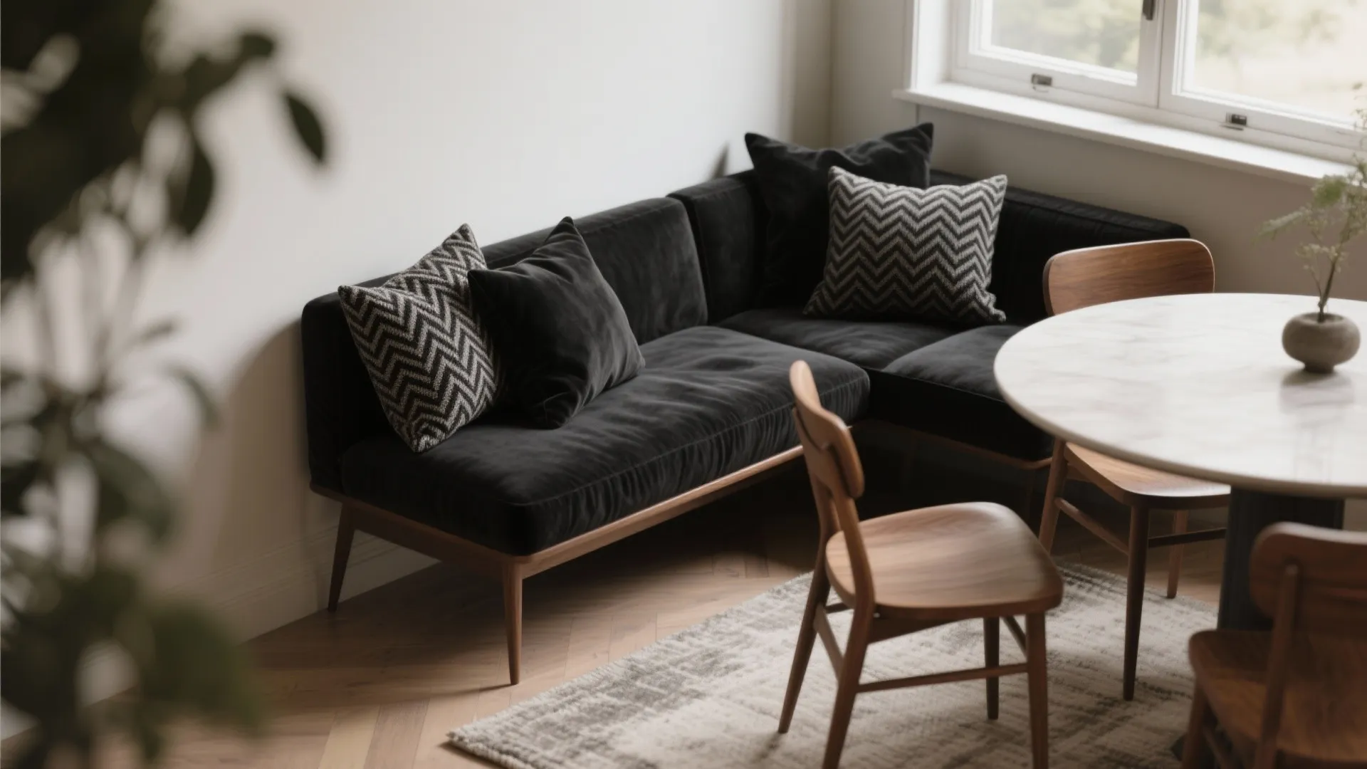 Dining nook showing black 18 x 16 cushions in varied textures (linen, herringbone, velvet) paired with warm wood chairs.