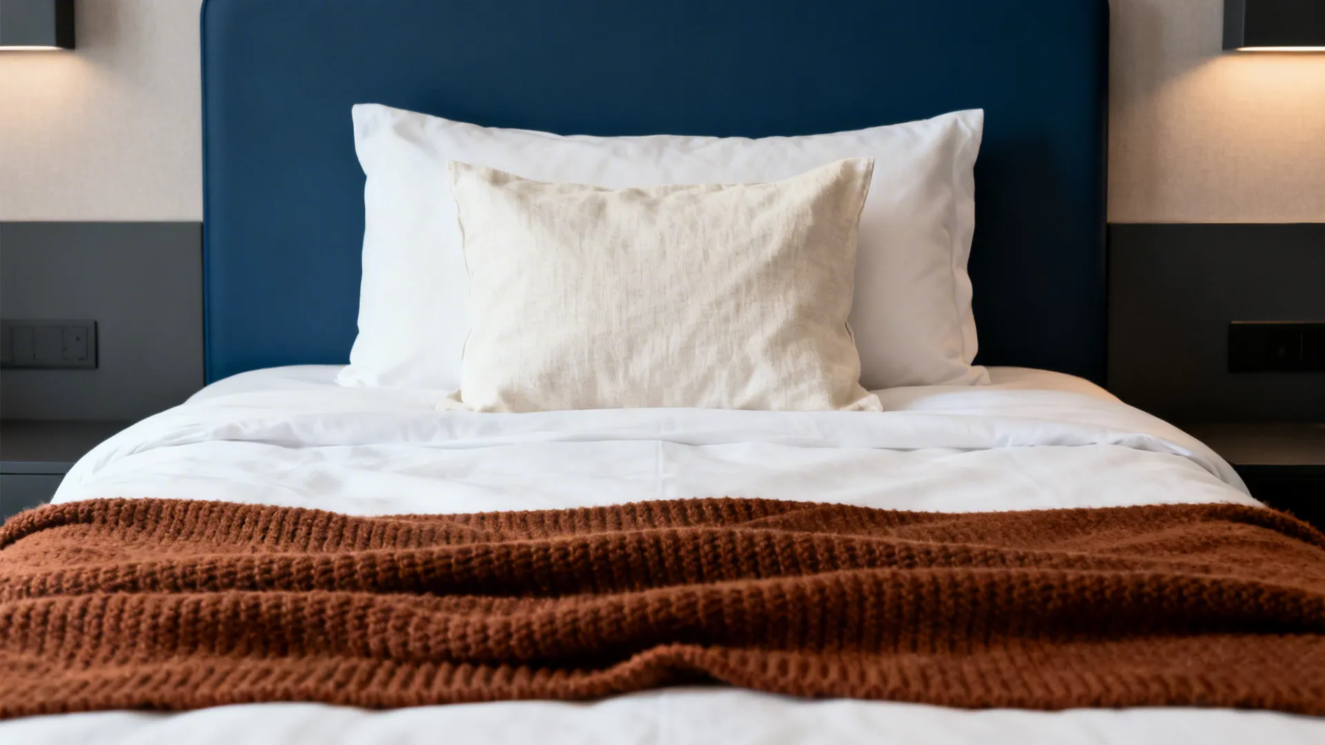 Crisp hotel bed with a whiskey knit throw at the foot and a natural linen pillowcase layered on top.