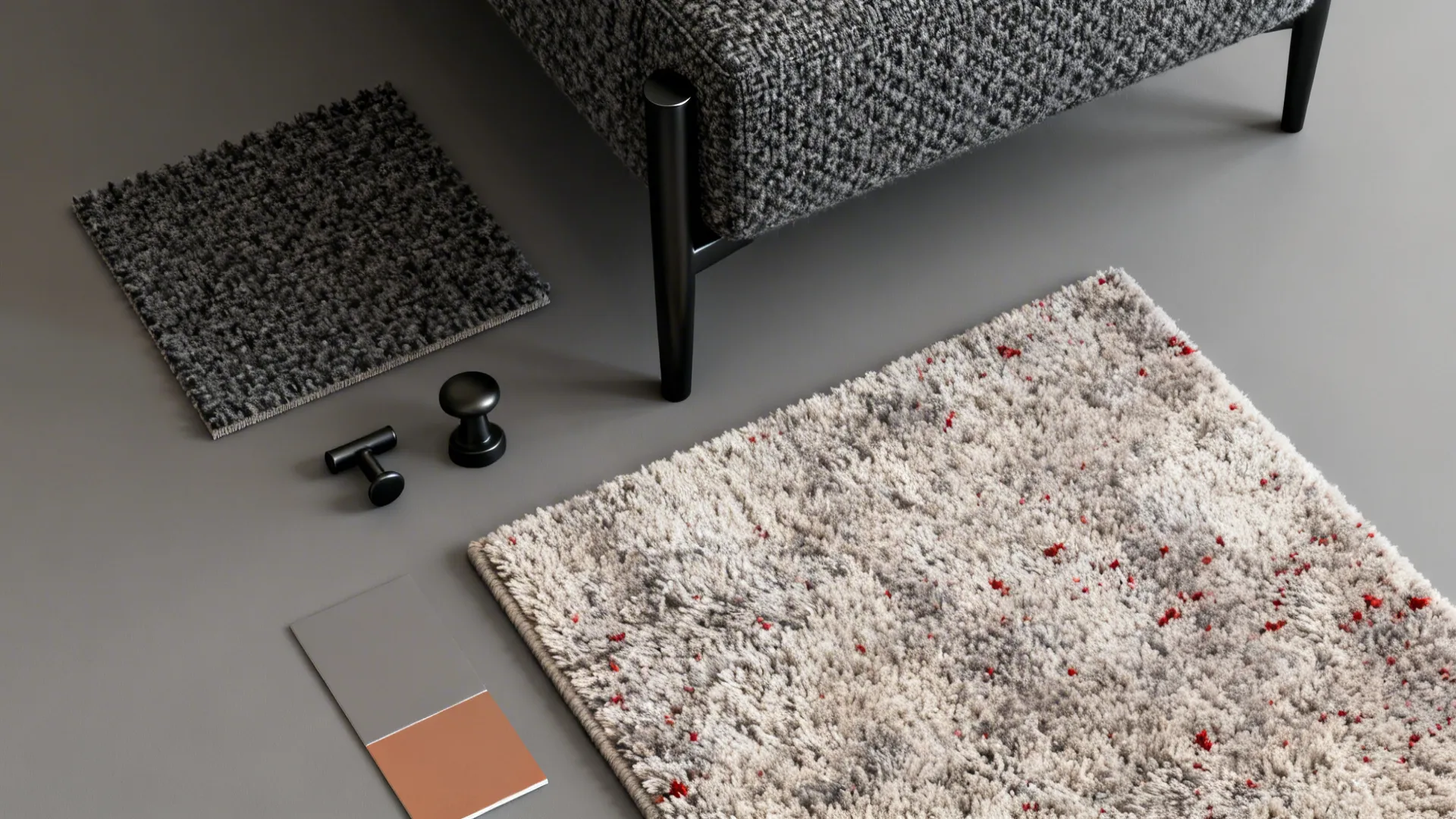 Flatlay of boucle fabric, matte black metal sample and high-pile rug with red flecks.