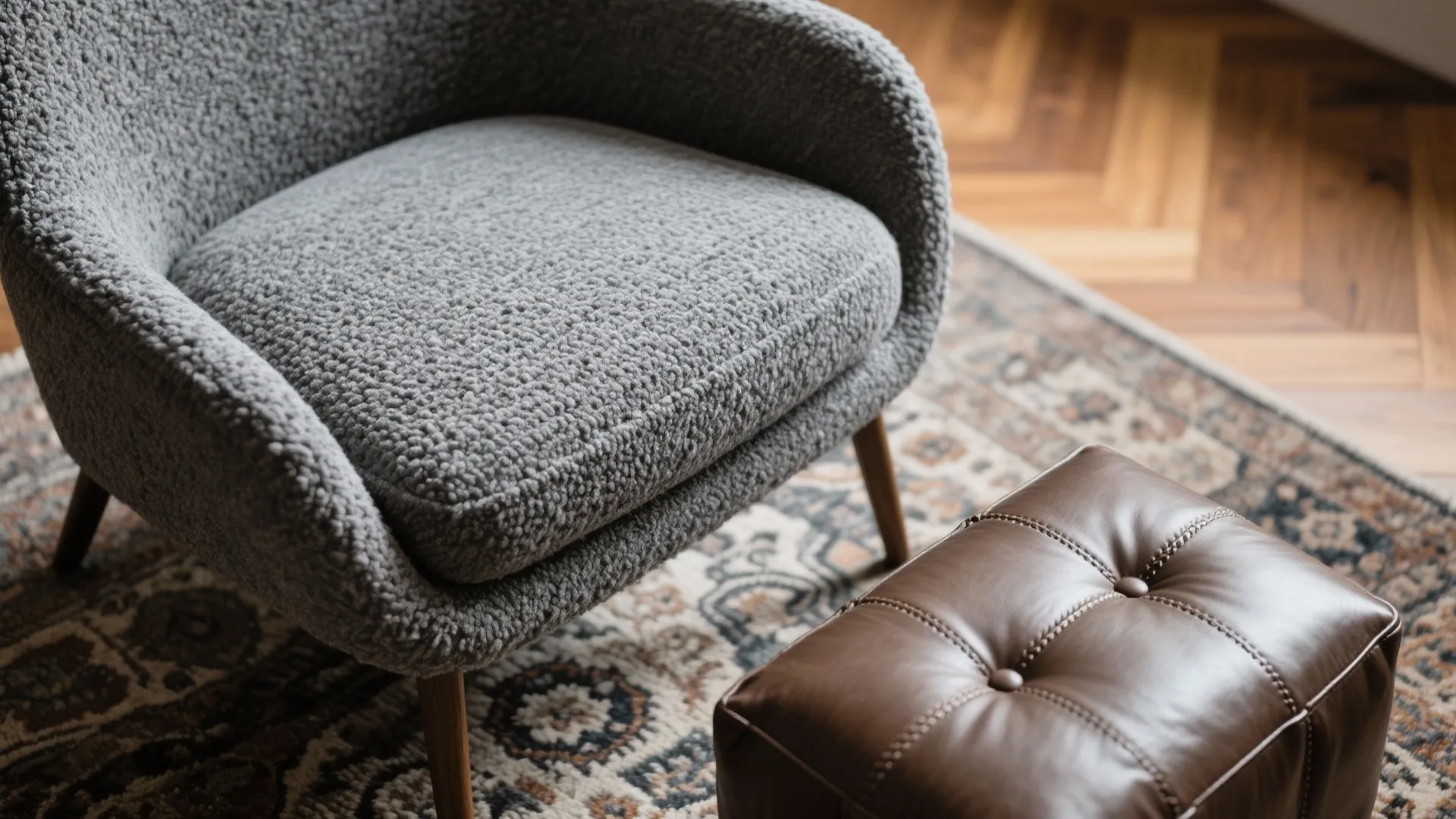 Close up of a grey textured armchair next to a brown leather footrest on rug
