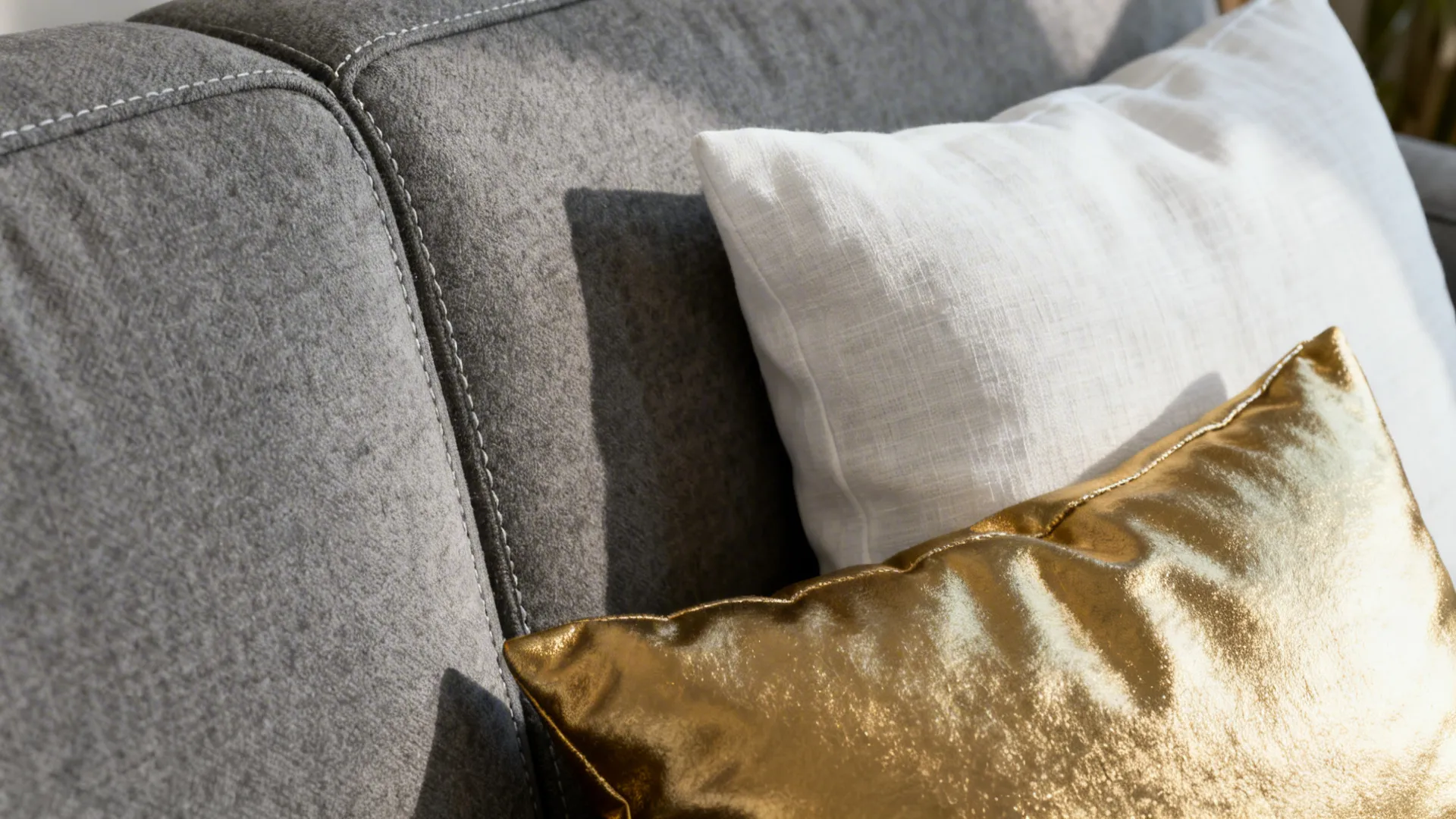 Close-up of matte gray upholstery, white linen cushion and metallic gold throw cushion