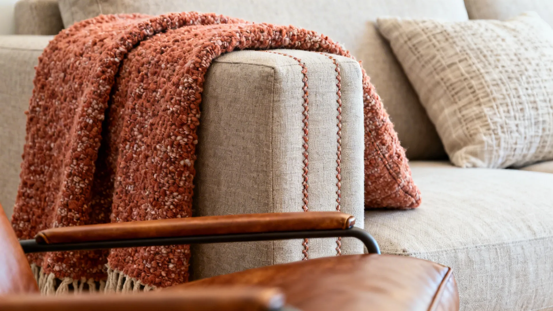 Close-up of bouclé throw, linen cushion, and leather accent chair textures beside a sofa.