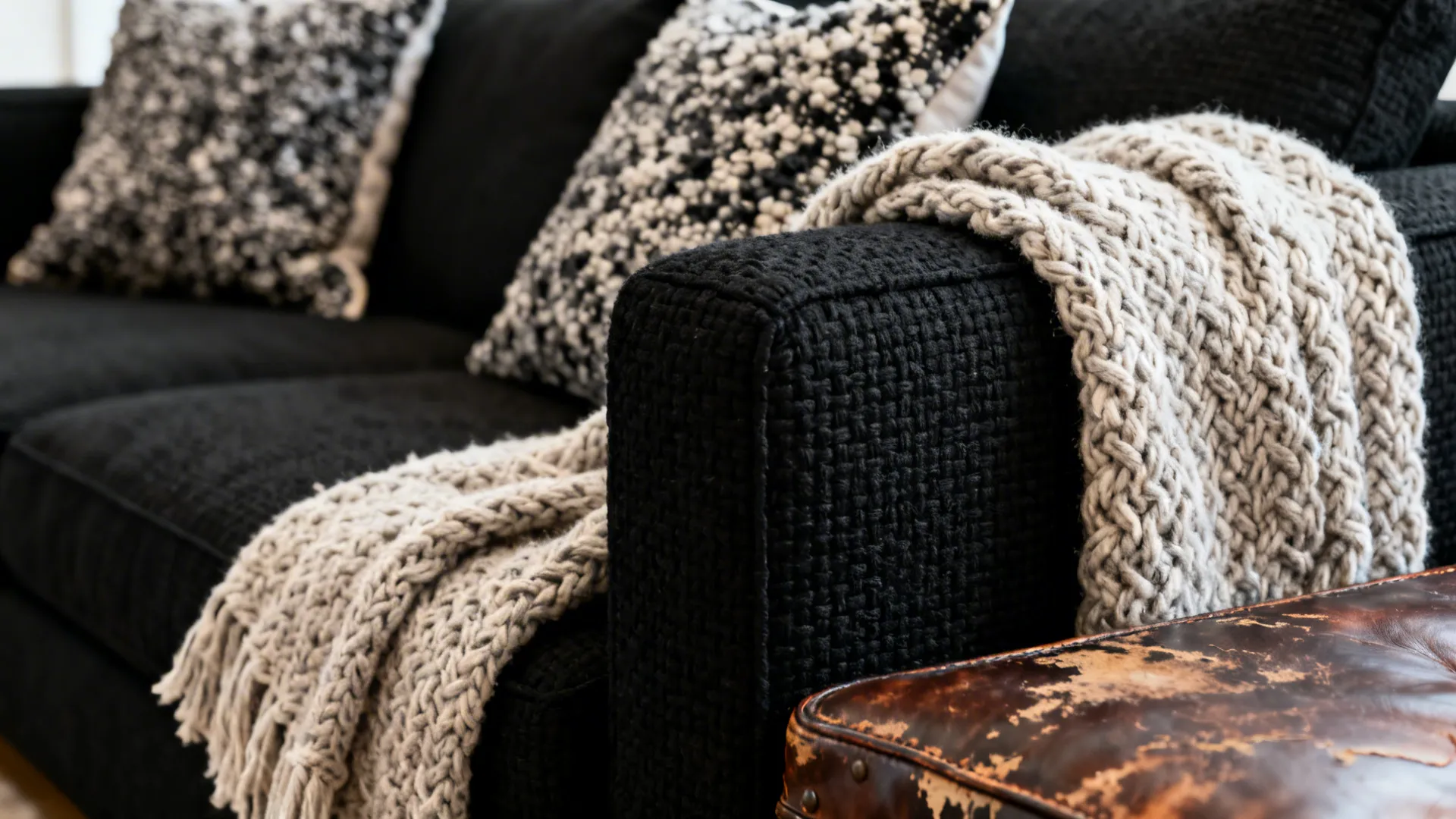 Close-up of boucle pillows, chunky knit throw and black sectional fabric showing rich textures.