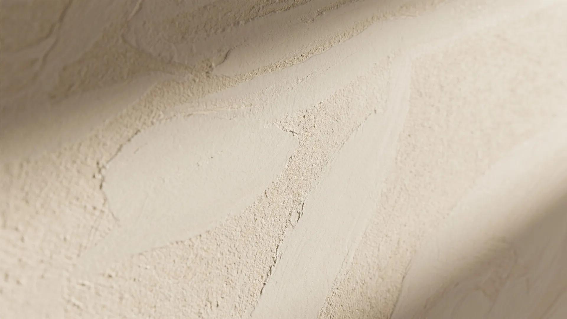 Close up view of light beige textured wall surface showing rough paint details and soft shadows