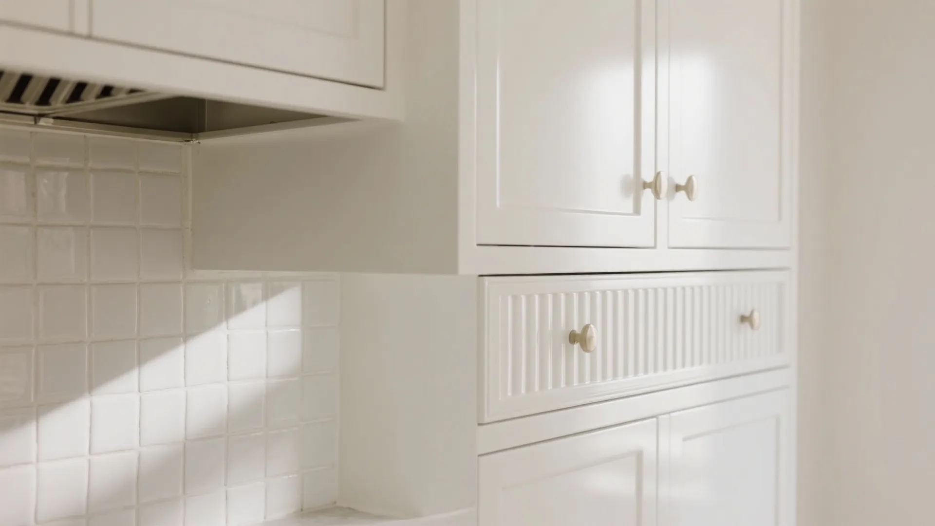 Close up of white kitchen cabinets with gold knobs white square tiles and fluted drawer