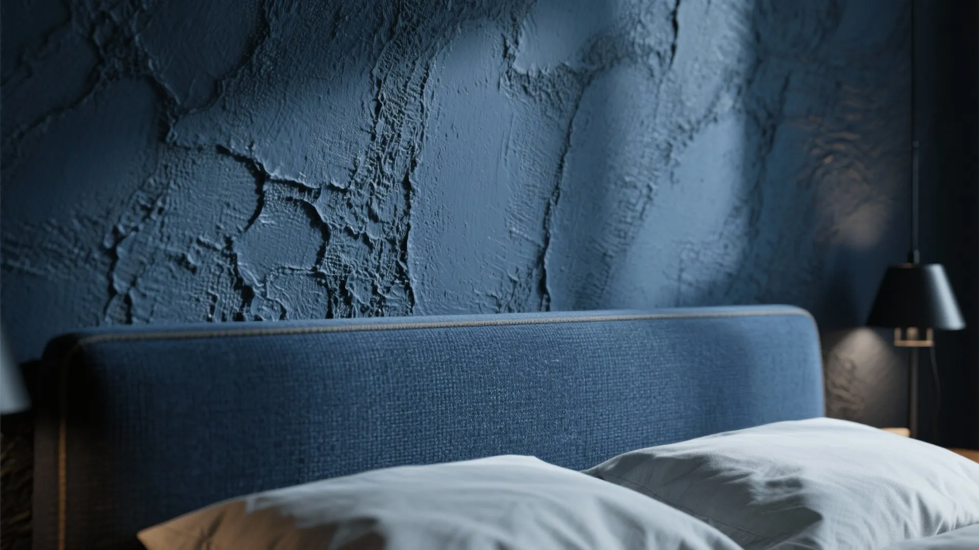 Close up of blue fabric bed headboard with white pillows against dark blue textured wall