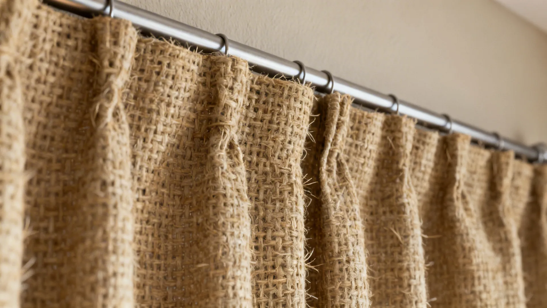 Thick brown textured fabric curtain hanging from a silver metal rod with several small rings