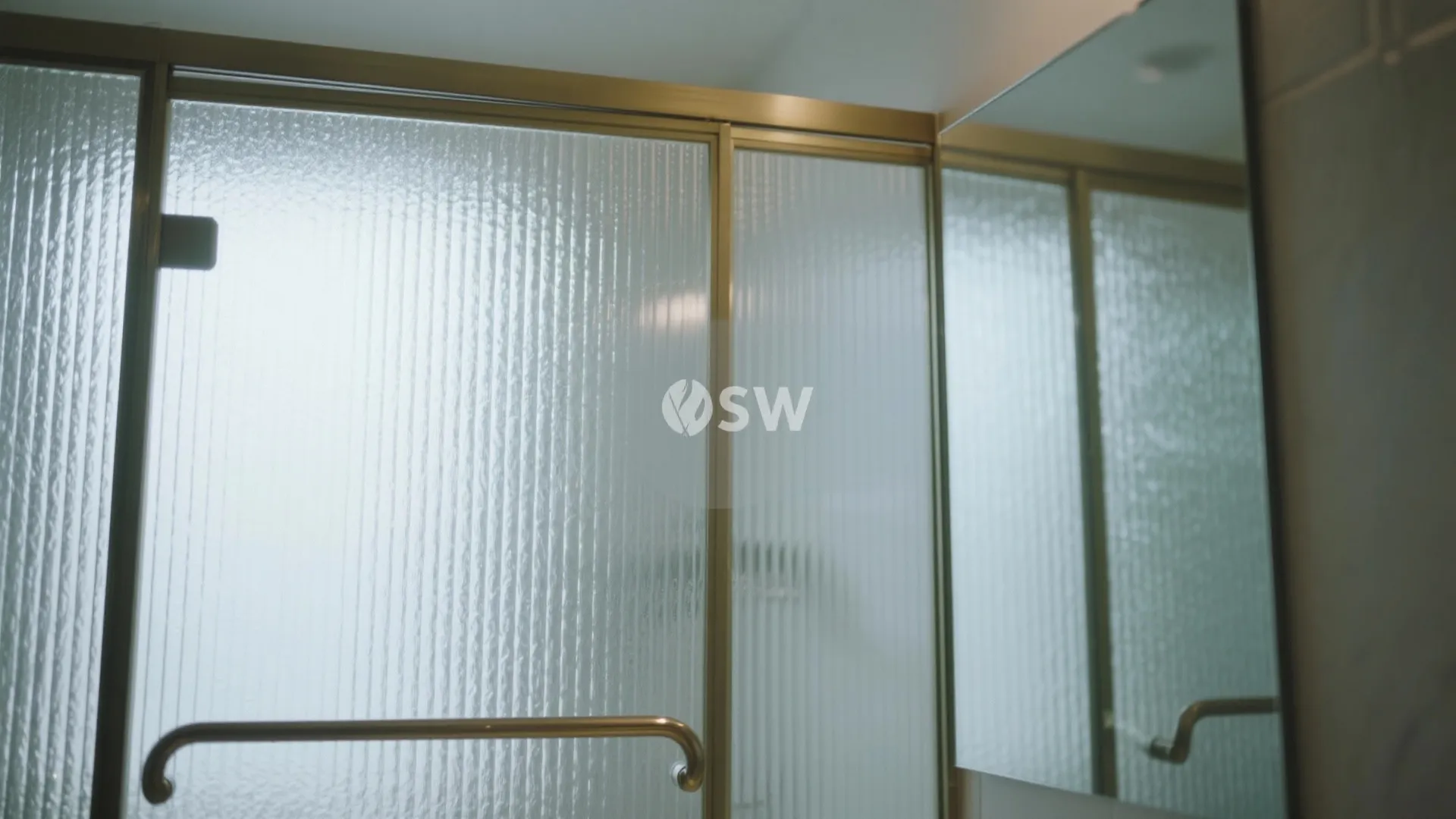 Close up view of textured glass shower door with gold frame in a modern bright bathroom