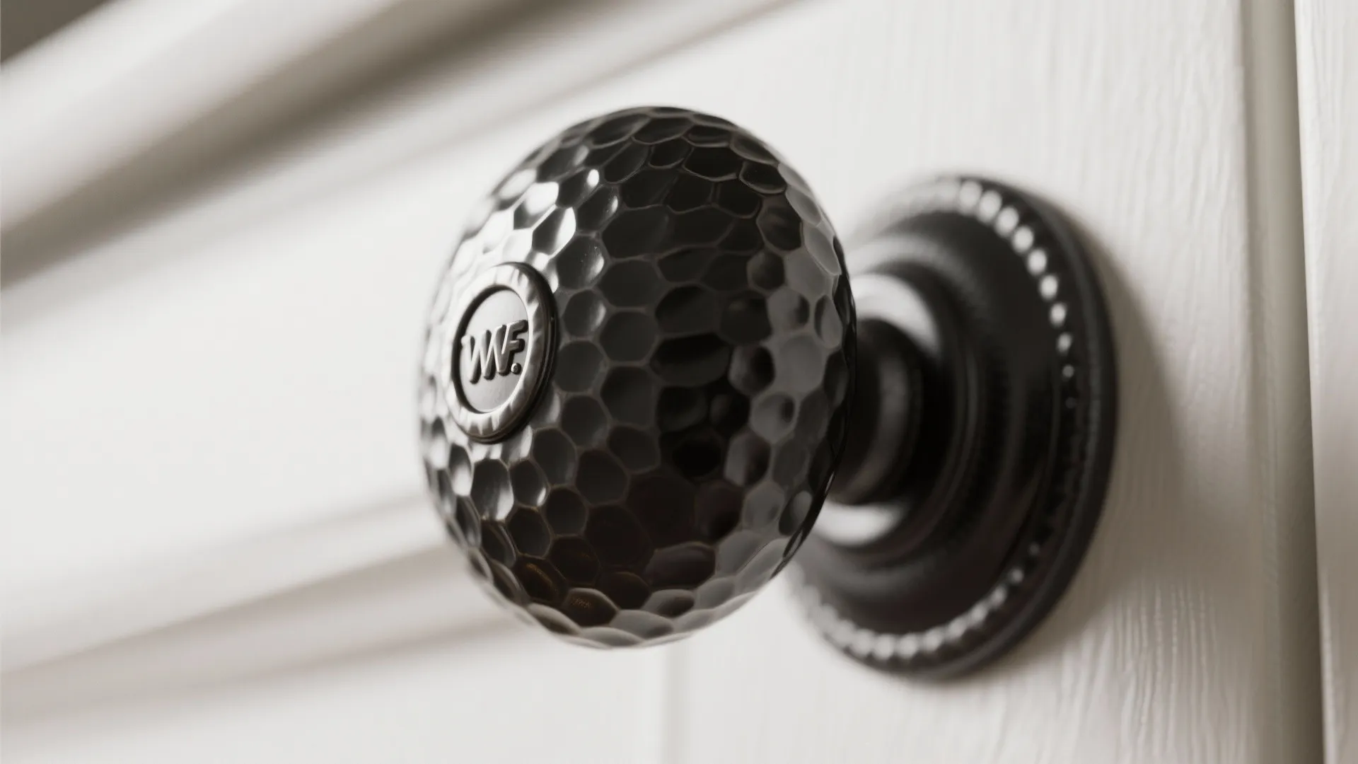 Close up of a textured black round door knob installed on a white wooden cabinet door
