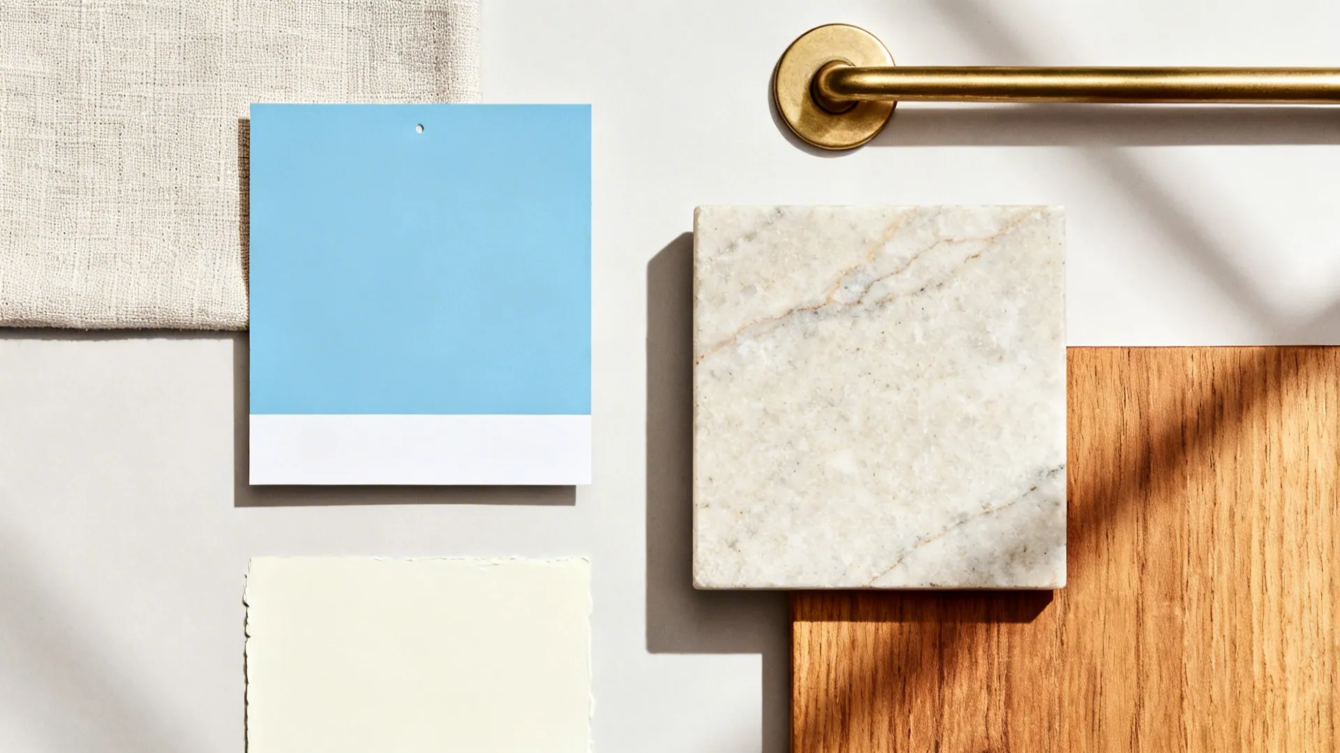 Flatlay with sky-blue paint, linen, honed stone, matte brass, oak, and creamy white.