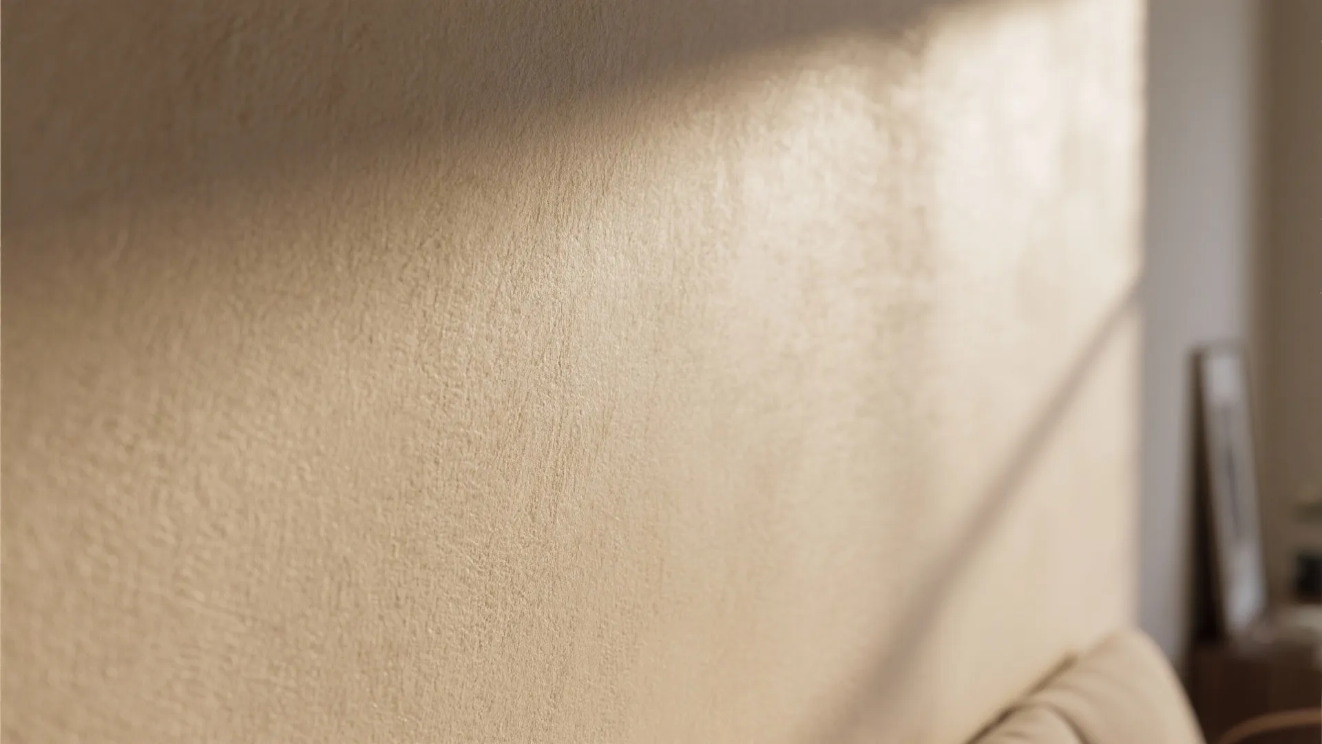 Close up of beige textured wall paint with soft sunlight and shadows in a room