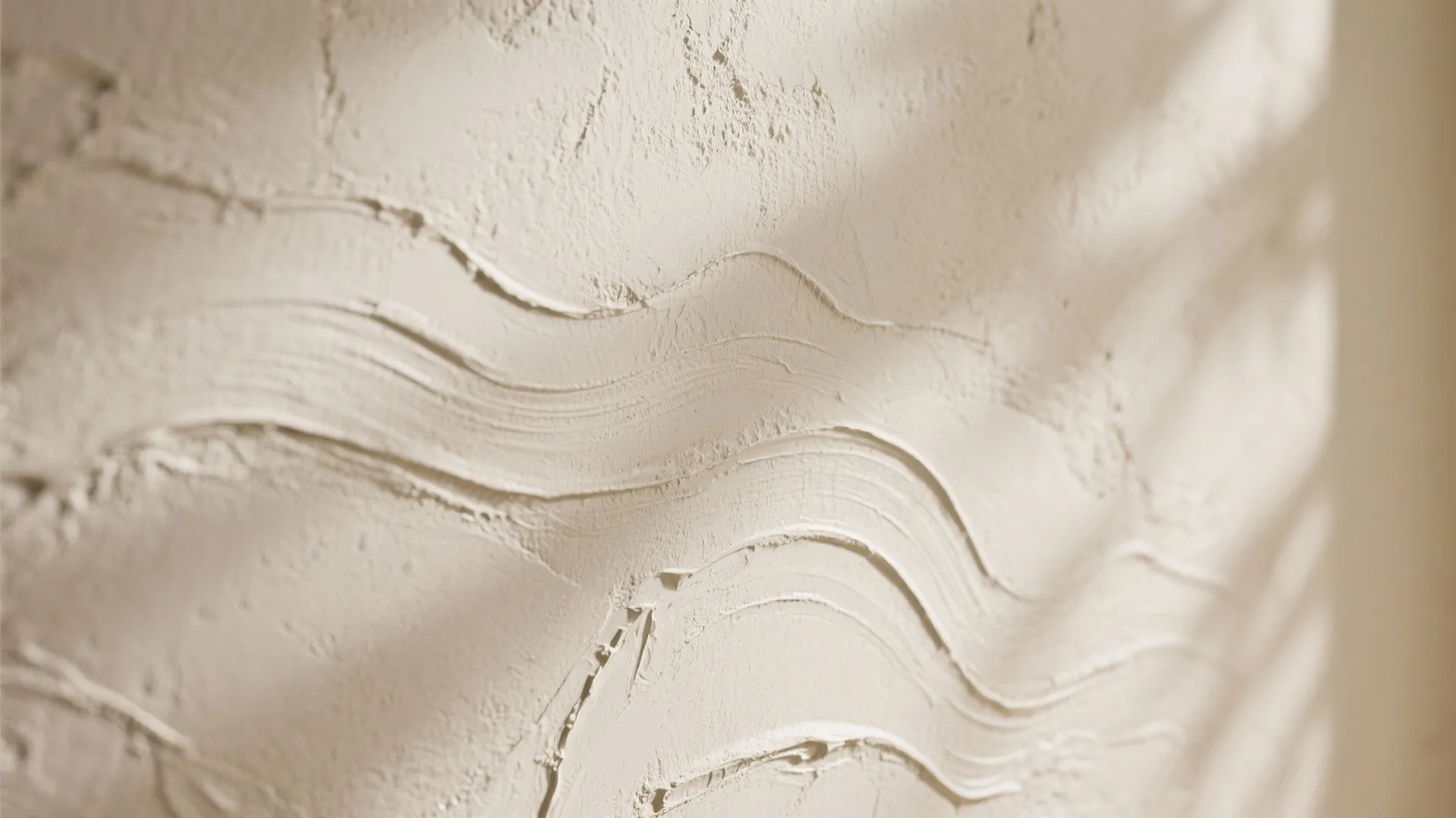 Close up view of beige textured wall plaster with wavy patterns and soft shadows from window