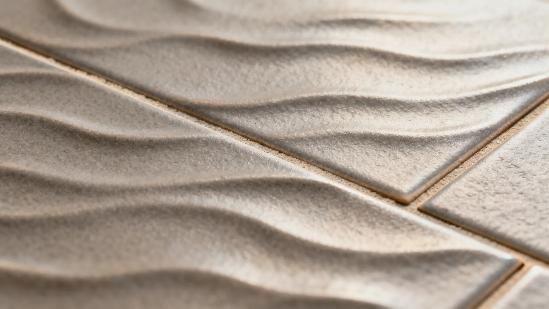 Close-up of warm gray ripple-textured tile with clean grout showing micro-shadows and tactile detail.