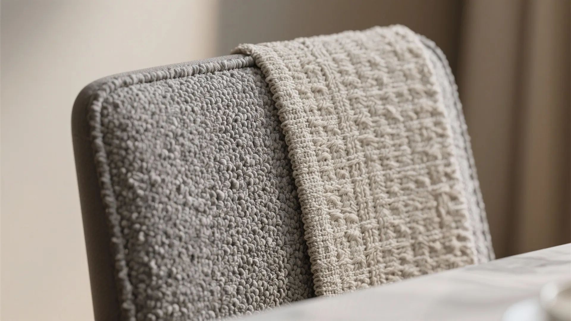 Close up view of a grey textured fabric chair back with a cream woven blanket