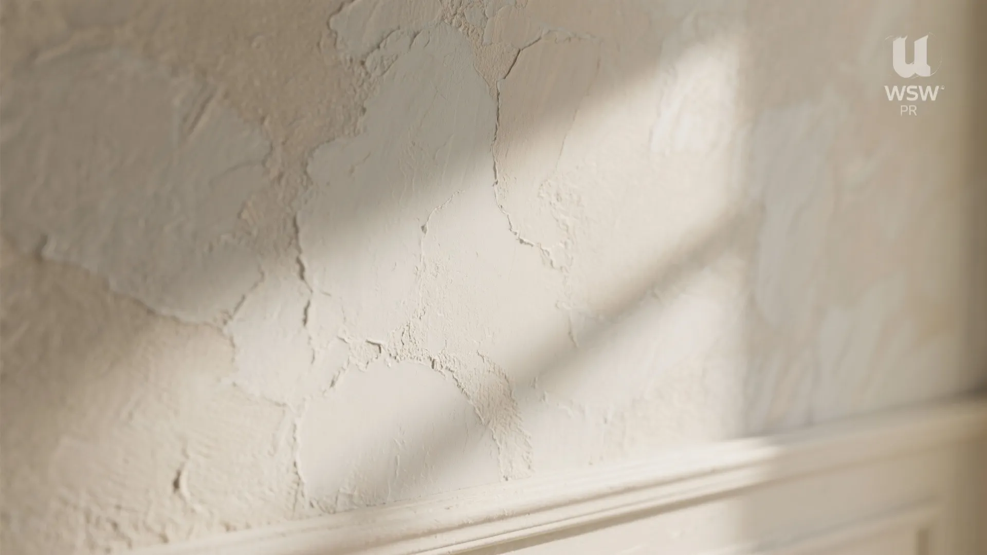 Close up view of beige textured plaster wall with soft shadows and white wall panel