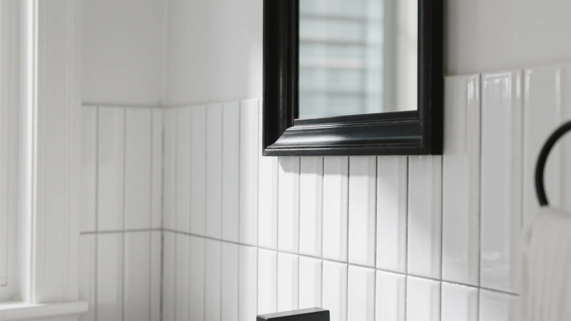 Close up of white vertical wall tiles with a black framed mirror and towel holder