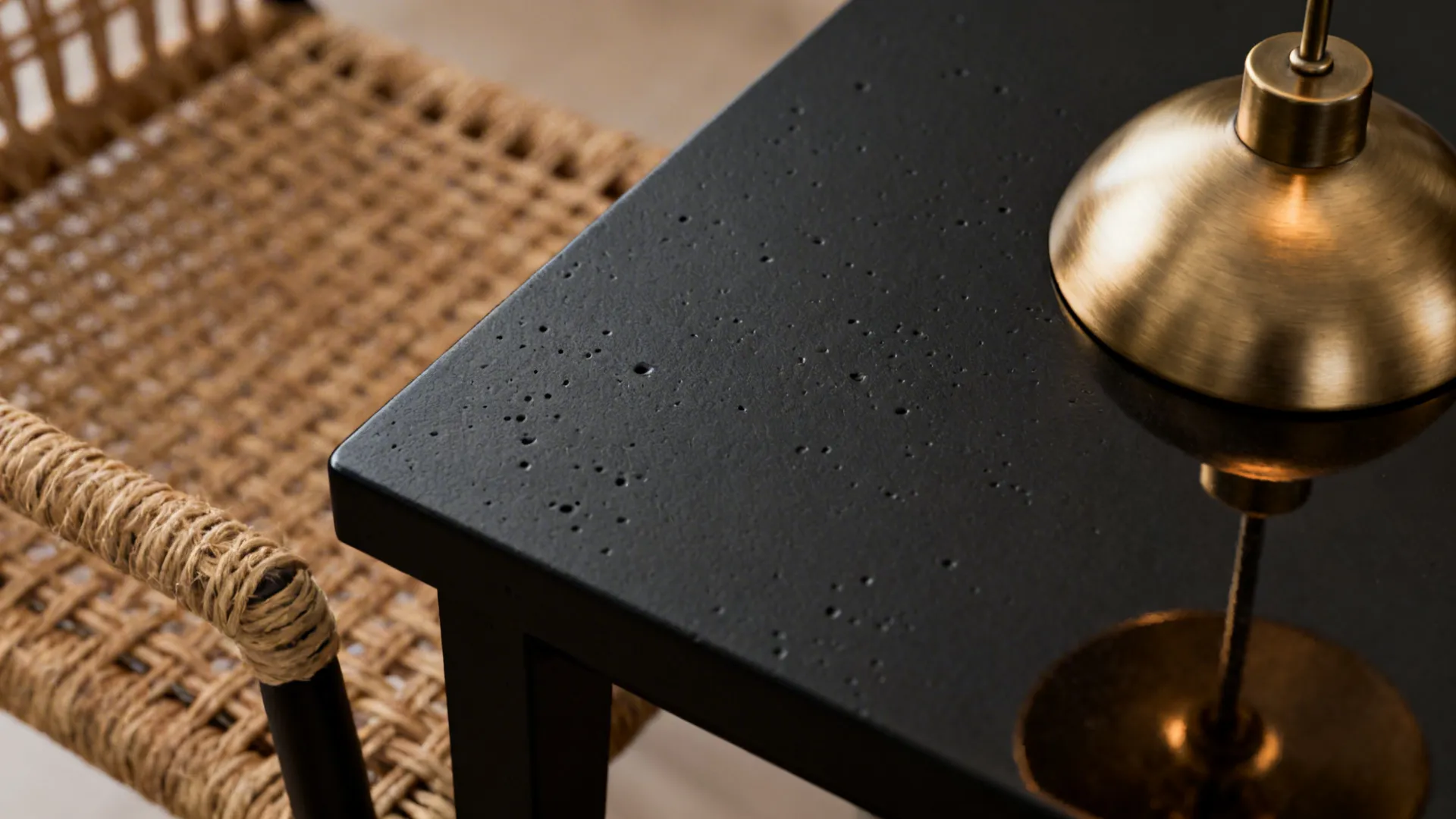 Close up of textured black table surface with gold light fixture and woven wicker chair
