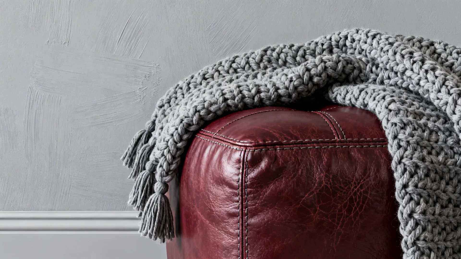 Close-up of burgundy leather ottoman, knit grey throw and matte grey wall textures