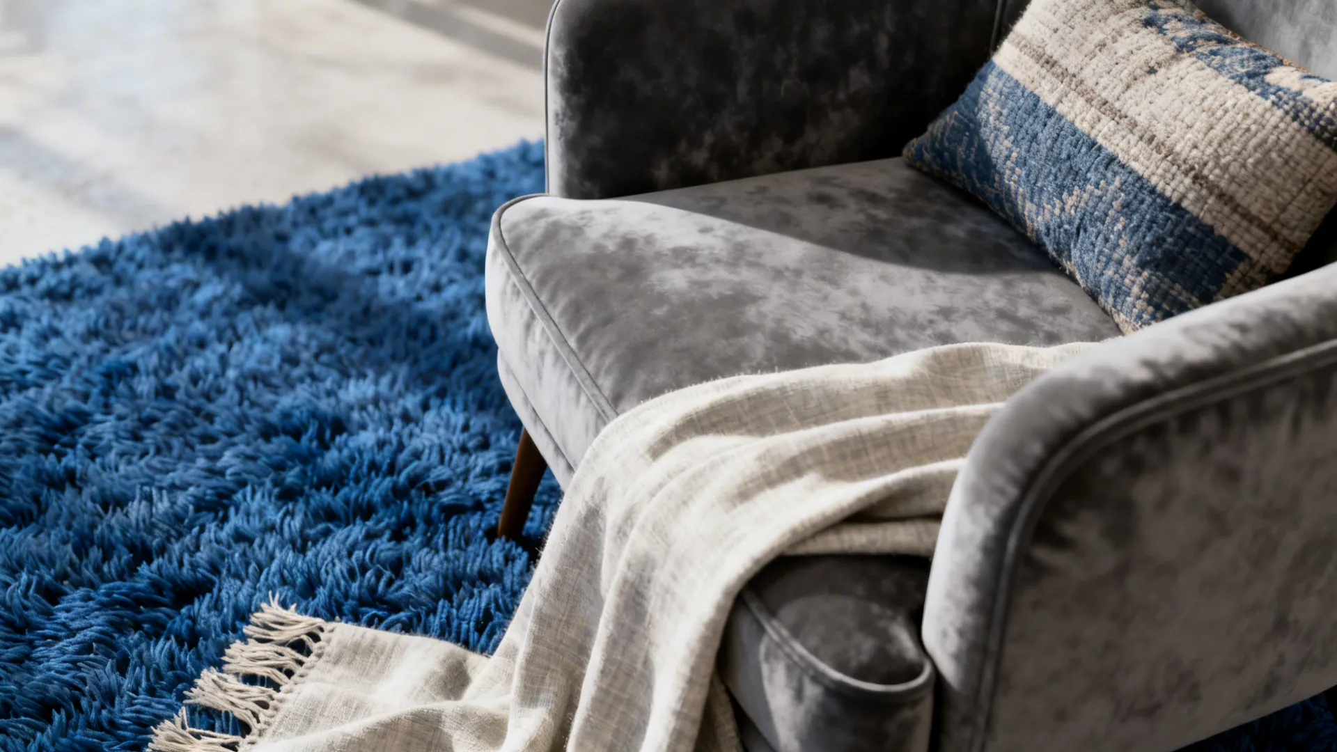 Close-up of grey velvet armchair, royal blue wool rug and linen throw showing contrasting textures.