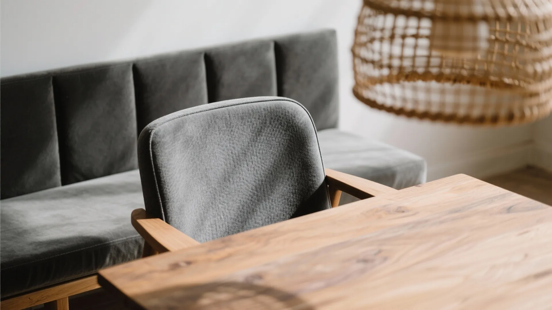 Modern grey chair and wooden dining table with a grey sofa and woven ceiling light