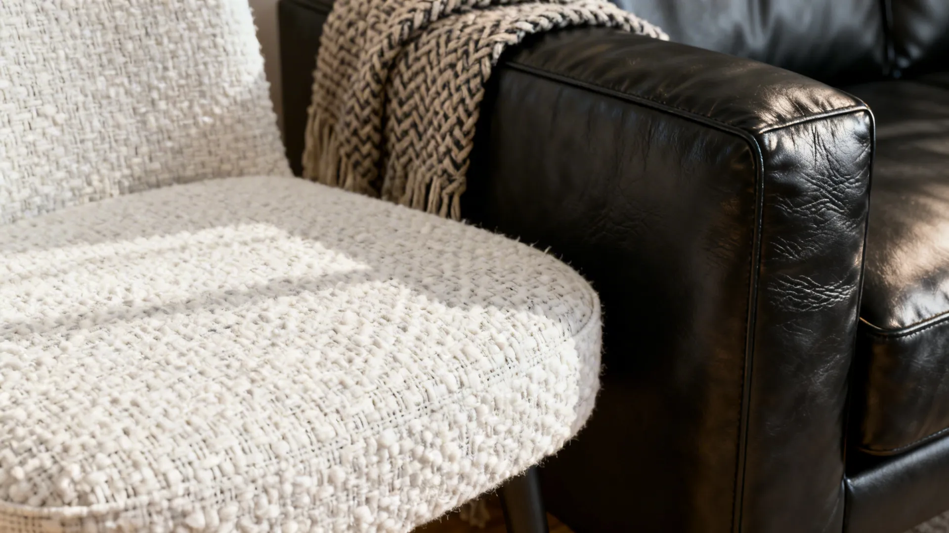 Close-up of white boucle chair next to a black leather sofa showing textured contrast and warmth.