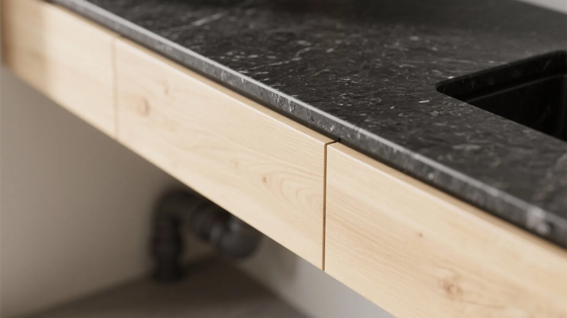Close up of a black marble stone cabinet top with thin edge and light wood drawers