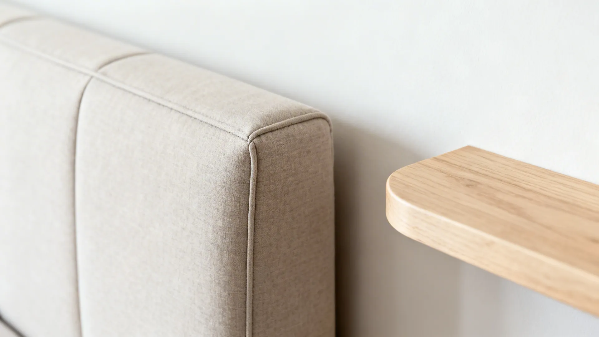 Detail of a tight-back sofa’s crisp tailoring beside a light wood floating shelf.