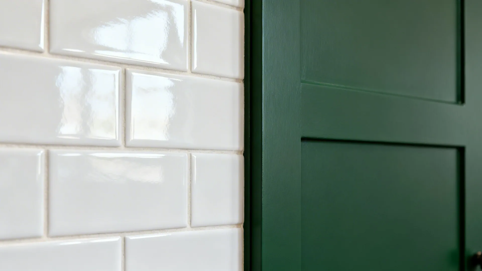 Glossy white wall tiles next to a dark green kitchen cabinet door with matte surface