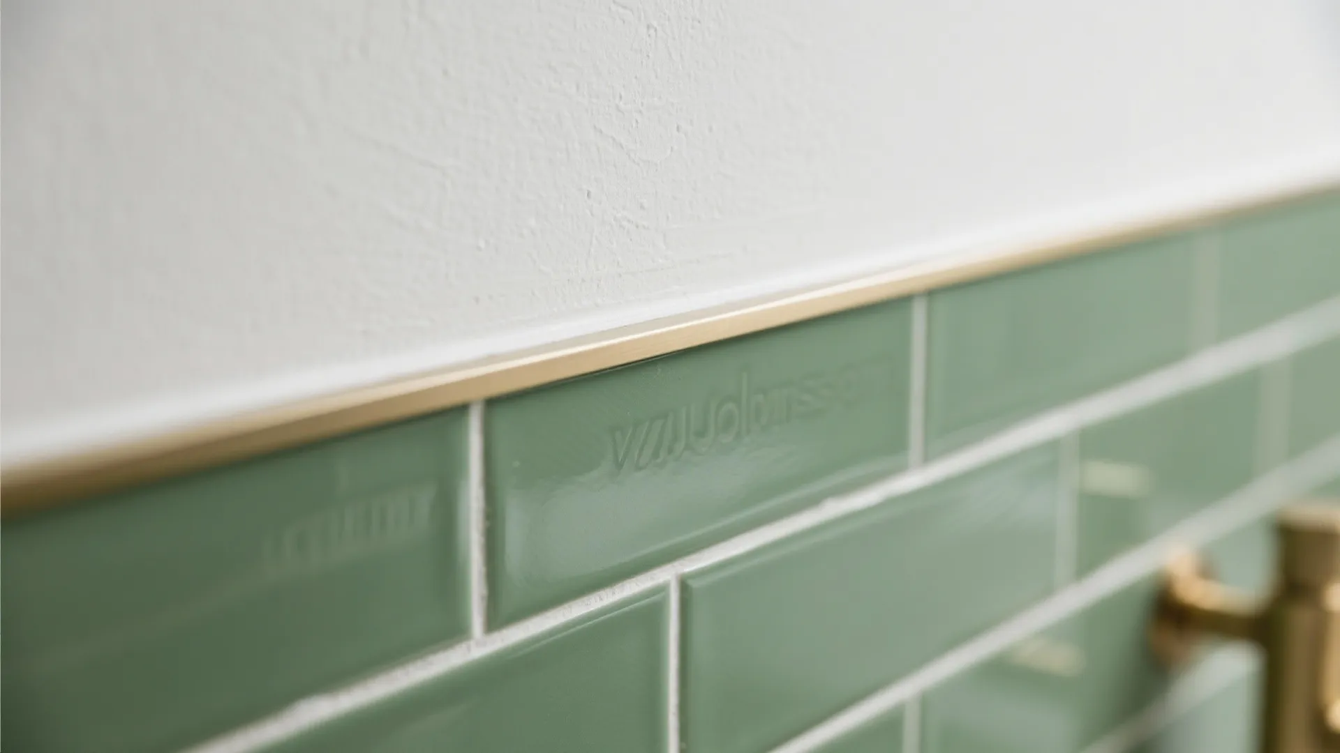 Close up of green wall tiles with gold metal trim meeting a white textured plaster wall