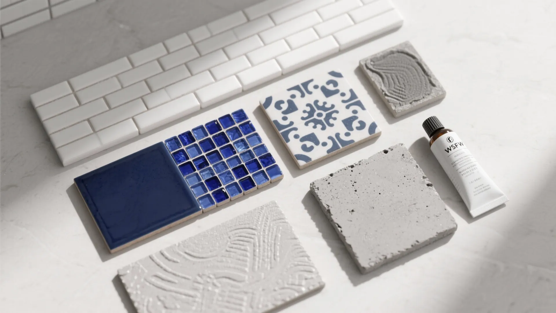 Flatlay of white and blue tile samples, grout swatch and sealer for bathroom planning.