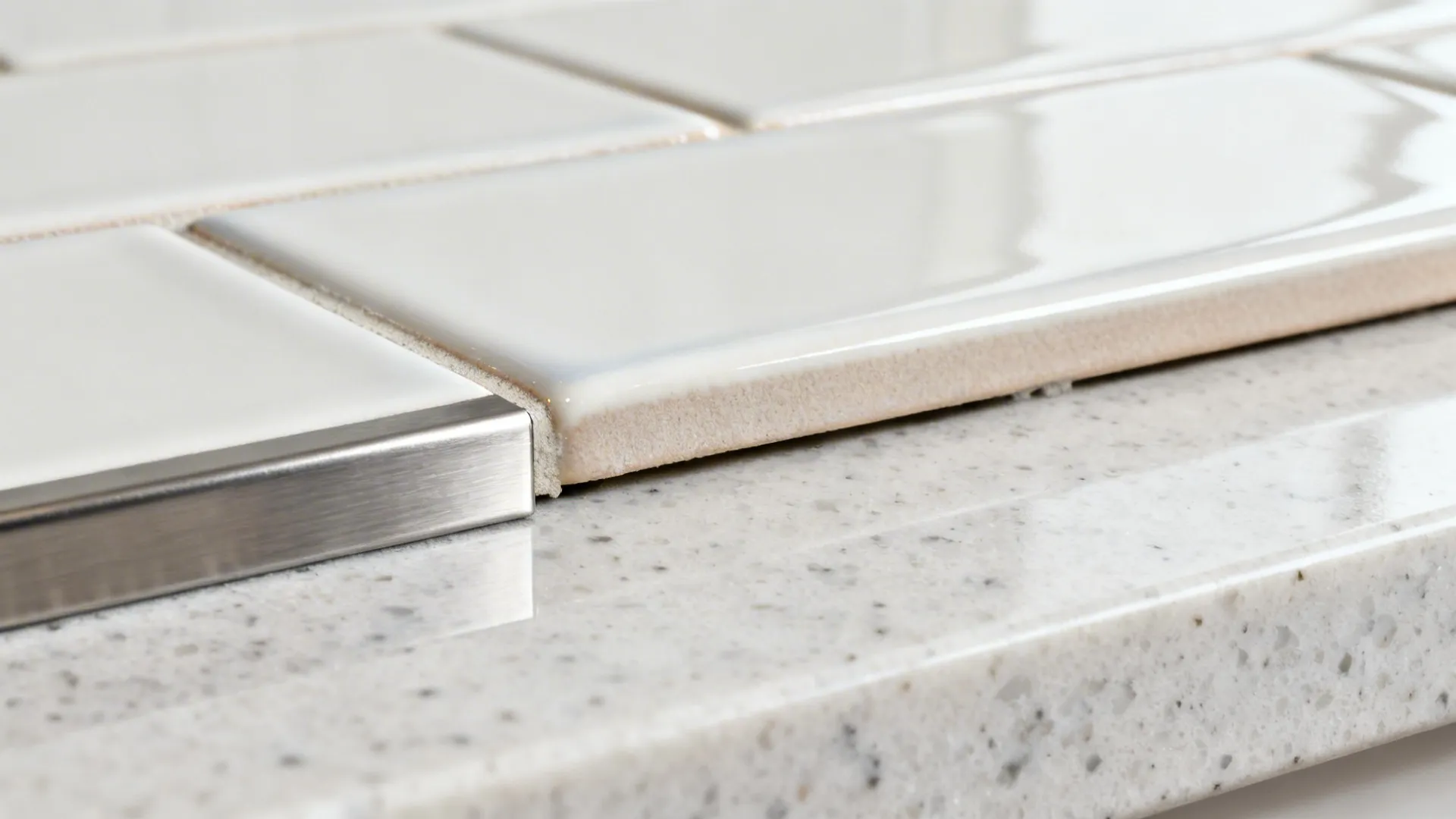 Macro of subway tile edge meeting metal profile trim with tight grout joint.
