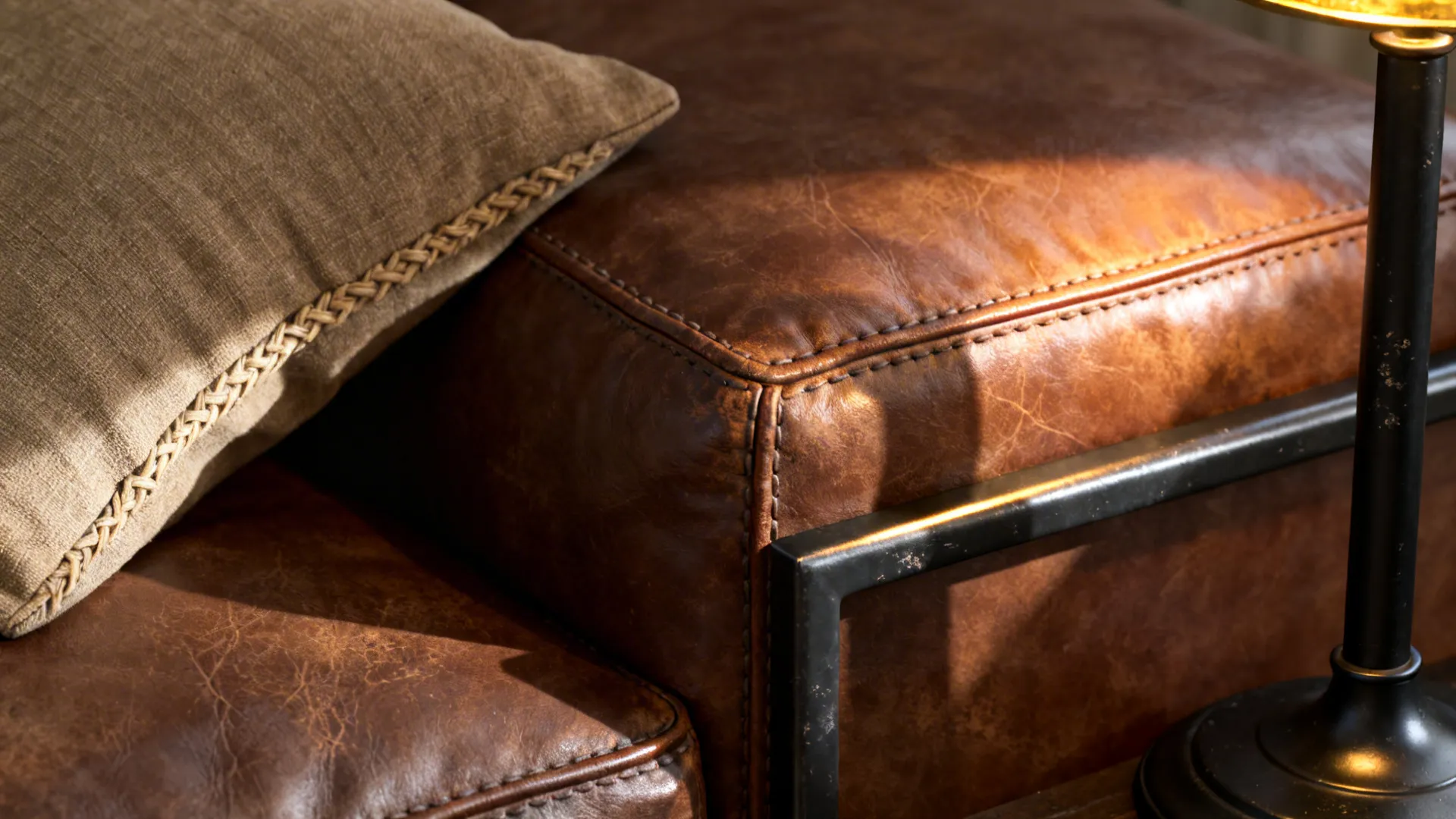 Close-up of tobacco leather sofa texture and matte black metal leg with linen cushion.
