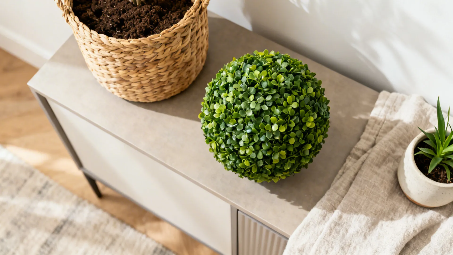 Small green round plant on a grey cabinet next to a woven basket and pot